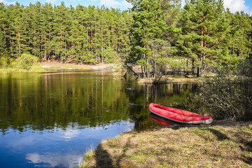 Red inflatable kayak near the bank of the forest river.