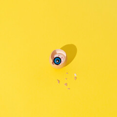 Cracked eggshell with evil eye in it on vivid yellow background.  Halloween celebration concept, square composition with copy space.