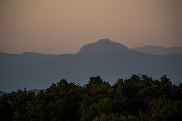 imagen de una montaña con las últimas luces del día, el cielo naranja y el paisaje con distintas intensidades