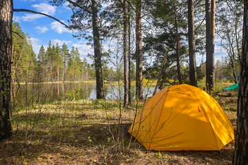 A yellow tent on the bank of a forest river.