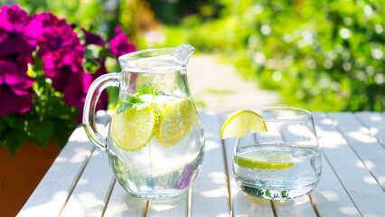 A pitcher of lemonade and a glass on a table in the garden