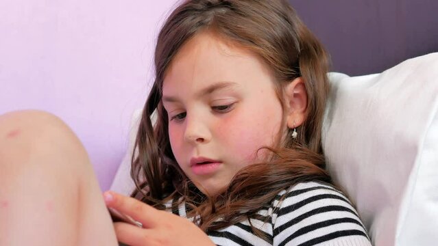 A beautiful little girl with a tablet in her hands, looking through information on the Internet, using voice messages on the tablet to search for information. Technology and children.