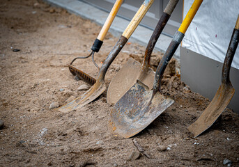 Dirty used shovels and a rake lean against a wall during a work break at a new home construction...