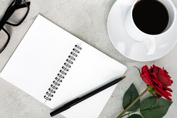 Notebook with coffee, pen, reading glasses, roses on white marble table.