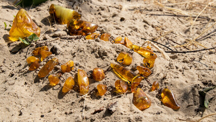 Handmade Baltic yellow amber necklace on the sand.  Transparent amber jewelry in the sun.