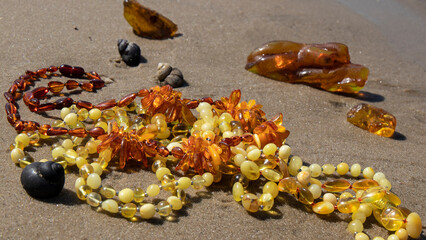 Colorful yellow and orange Baltic  amber beads on sand.  Isolated shiny  amber jewelry and amber stones.