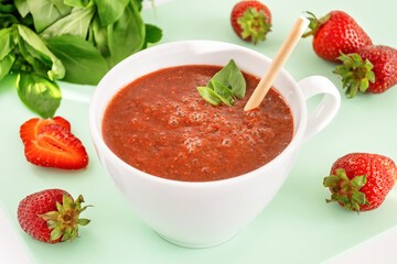 Homemade red strawberry smoothie with basil green leaves and paper straw. Summer beverage with fresh fruit and greenery.