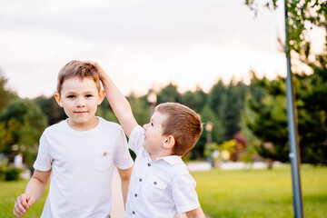 A little boy measures his older brother's height with his hand in a park in nature. Children play together.