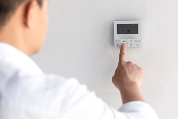 Asian businessman in office heat, chooses cooling mode of air conditioner on control panel on white...