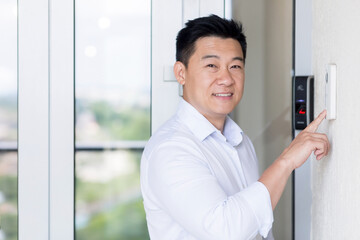 Asian businessman portrait, man walks into modern office, uses doorbell with fingerprint lock, man...
