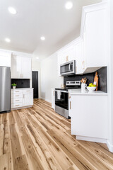 A modern farmhouse kitchen with white cabinets, black hexagon tile backsplash, wood plank floors...