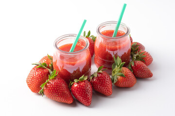 Strawberry juice in glass cup next to juicy strawberries, isolated on white background.