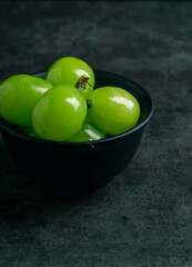 A branch of green juicy grapes in a plate with copy space. Black background. Front view. Place for writing. Suitable for Summer.