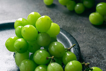 A branch of green juicy grapes in a plate with copy space. Black background. Front view. Place for writing. Suitable for Summer.