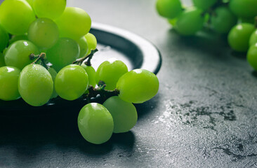 A branch of green juicy grapes in a plate with copy space. Black background. Front view. Place for writing. Suitable for Summer.