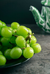A branch of green juicy grapes in a plate with copy space. Black background. Front view. Place for writing. Suitable for Summer.