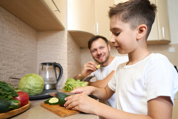 Parent watching his son cutting vegetable in kitchen