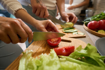 Person cutting tomatoes on chopping board near lettuce