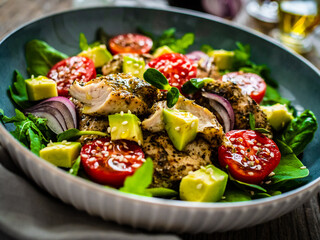 Tasty salad - fried chicken breast, avocado, mini tomatoes and fresh green vegetables on wooden background
