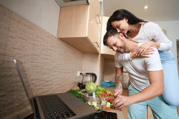 Tender wife hanging on man neck during cooking in kitchen