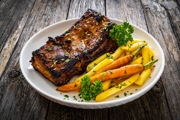 Tasty grilled ribs with french fries and caramelized carrots  on wooden table