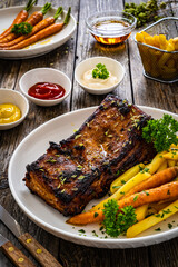 Tasty grilled ribs with french fries and caramelized carrots  on wooden table