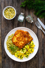 Breaded fried pork chop with bone, boiled potatoes and  boiled cabbage on wooden table
