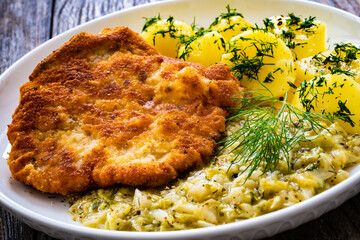 Breaded fried pork chop with bone, boiled potatoes and  boiled cabbage on wooden table
