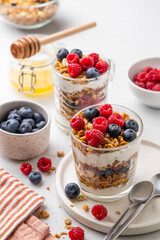 Granola with yogurt in glass served with fresh raspberry, blueberry and honey. Homemade oatmeal muesli. Vegetarian breakfast, healthy eating concept. Selective focus.