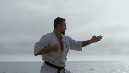 Man making karate kicks on seacoast close up. Athlete training fighting skills.