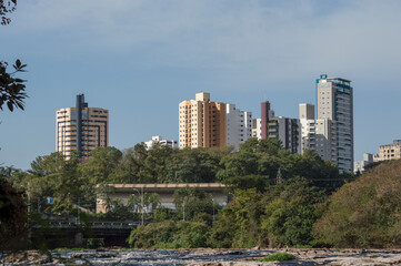 City in the distance with buildings, towers, blue sky, many trees below and rocks from the river, Piracicaba SP Brazil.