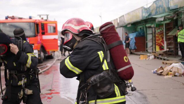 Group of firefighters preparing for a drill, firefighter in protective gear with a helmet on his head checking his equipment, a fire truck in the background is also visible