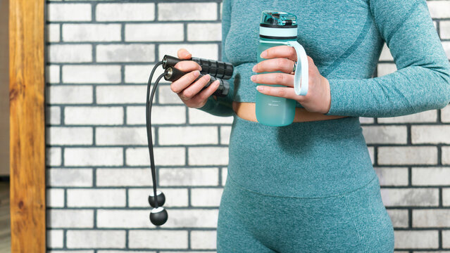 Home fitness workout concept. Cordless jump rope and water bottle in hands of a women in sportswear. Modern sports accessories for a healthy lifestyle.