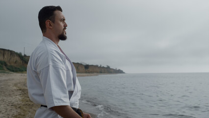 Sporty man doing karate exercise on beach close up. Athlete practicing taekwondo