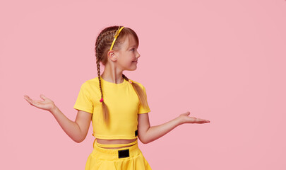Portrait of cute toddler girl child with two funny pigtails over pink background. Points hands to the left side. Advertising childrens products
