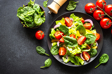 Green salad with fresh vegetables and green leaves at black background. Top view with copy space.