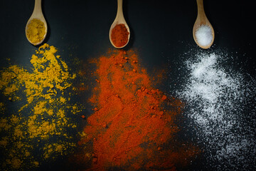 Three wooden spoons with spices - salt, curry, and ground paprika on a black background