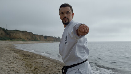 Karate man training fighting skills on sandy beach close up