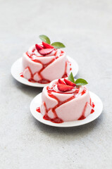 Vegan dessert. Strawberry cream pudding, Panna Cotta with sauce, in the shape of a rose, on a plate. Light grey background