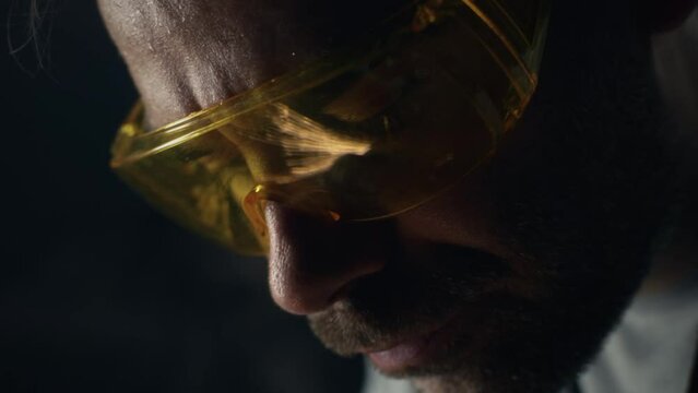Close shot of serious male worker in protective goggles metalworking in garage with professional equipment