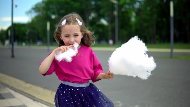 Two children in purple and yellow t-shirts eat cotton candy on a sunny summer day. Little girls enjoy sweets in the park.