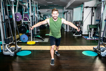 handsome muscular fitness guy trains at cable machine his triceps by pull wights with both arms and smile satisfied in camera while tough workout