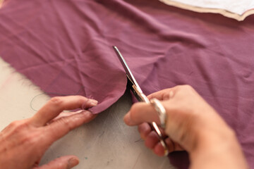 hands of a seamstress cutting a piece of fabric with a pair of scissors