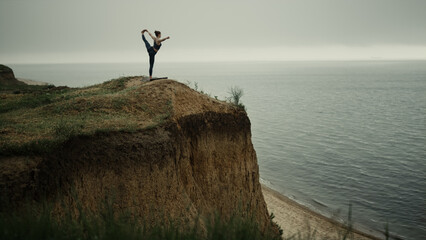 Athlete woman streching holding leg on beach hill. Girl practicing yoga near sea