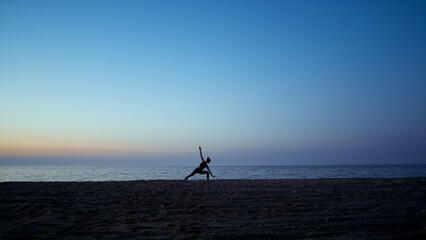 Silhouette yoga woman training warrior asana in front beautiful sunset sky.