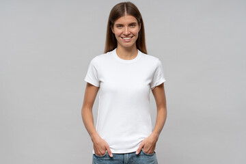 Young woman in casual white t-shirt standing with hands in pockets - obrazy, fototapety, plakaty