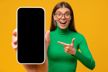 Excited shocked young woman pointing finger to blank phone screen with copy space for app