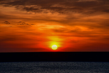 The sunset is bright with the big yellow sun below the sea surface, by the dam.