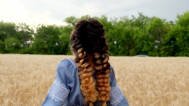 A beautiful smiling young woman in traditional Ukrainian clothes runs through the golden wheat field, spins around, enjoys outdoor recreation, freedom and carefree mood in the summer nature at sunset.