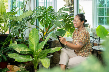 Obraz premium Young woman working with Tablet Laptop at Green house Garden Shop, Digital Nomad woman Remote working Online job or Teaching online Lifestlye Digital Nomad, Woman Freelance working freedom 